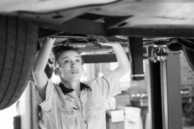 A woman is working underneath a raised car