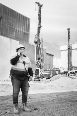 A woman in a hard hat is on a construction site using a phone