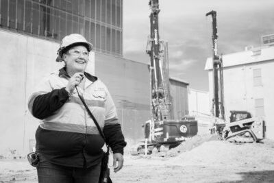 A woman in a hard hat is on a construction site using a radio